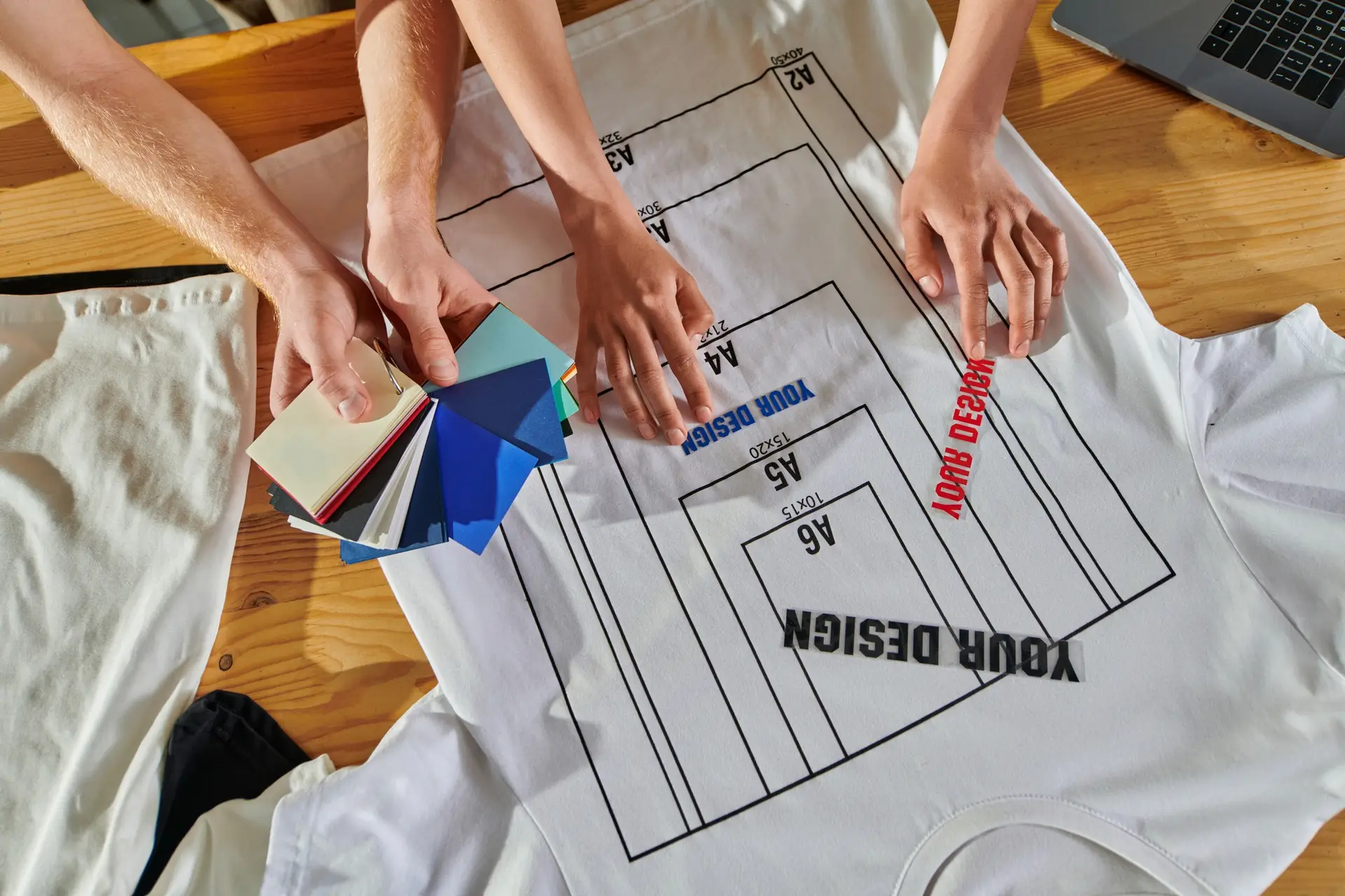 Top view of young multiethnic craftspeople holding color swatches and printing layers near laptop