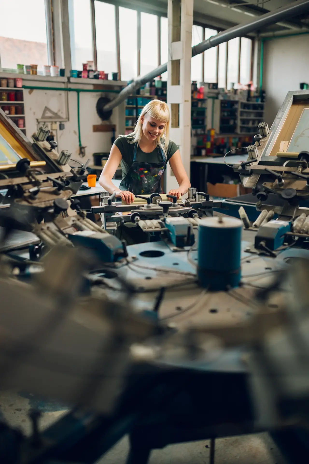 Young graphic worker is screen printing on carousel printing machine.